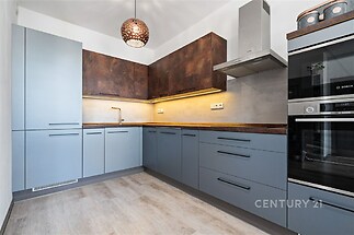 Moderní kuchyň s parketovou podlahou, stylovými vestavěnými spotřebiči a dřevěnou matnou úpravou skříněk.
