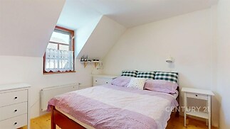 Světlá ložnice s dřevěnou podlahou, šikmým stropem a velkým oknem poskytujícím dostatek přirozeného světla, zařízená v moderním stylu.
