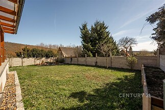 Zahrada s travnatou plochou, obklopená dřevěným plotem, s výhledem na okolní stromy a klidné přírodní prostředí.