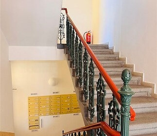 Schodiště s ozdobným kovovým zábradlím, dlažba s geometrickým vzorem, světlé stěny v historickém domě