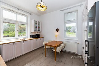 Světlá kuchyň s dlažbou, velkými okny a dřevěnými skříňkami nabízí moderní a funkční prostor pro rodinné vaření.