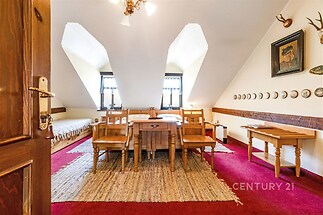 Podkrovní jídelna s červeným kobercem, dřevěným nábytkem a velkými střešními okny, které poskytují světlý a útulný prostor.