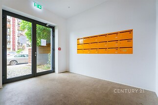 Vstupní hala s dlažbou, která vede k proskleným dveřím, nabízí moderní design. Poštovní schránky na stěně dodávají praktické využití prostoru.