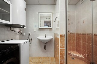 Praktická koupelna s dlažbou, sprchovým koutem a bílým nábytkem, nabízí moderní komfort a elegantní provedení pro každodenní použití.