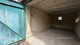 Praktická garáž s betonovou podlahou, zelenými plechovými vraty a malým oknem, ideální pro parkování nebo skladování v rekreačním objektu.