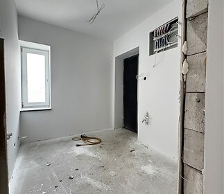 Světlá rekonstruovaná koupelna s betonovou podlahou a bílými stěnami, připravená k instalaci sanitárního zařízení, vybavena elektroinstalací.