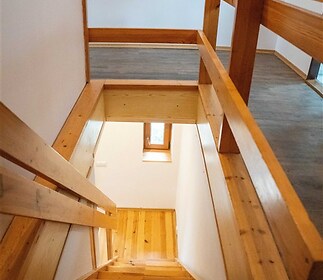 Schodiště s dřevěným zábradlím a parketovou podlahou, světlé dřevěné prvky dodávají moderní vzhled a prostornost.