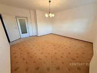 Světlý obývací pokoj s kobercovou podlahou, bílými stěnami a centrálním osvětlením, nabízí možnosti pro moderní úpravy.