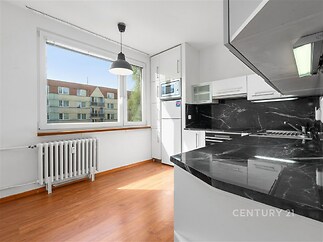 Moderní kuchyň s dřevěnou podlahou, velkými okny a černou mramorovou pracovní deskou poskytuje světlý a elegantní prostor k vaření.
