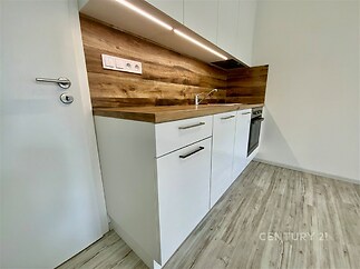 Moderní kuchyň s dřevěnými detaily, světlá parketová podlaha, vestavěné spotřebiče, čistý design.