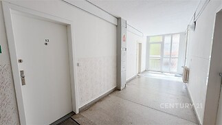 Předsíň bytového domu s dlažbou, bílými stěnami a velkými okny zajišťujícími dostatek světla, moderní a čistý design prostoru.