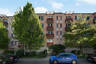 Moderní bytový dům s barevnou fasádou, balkonem a výtahem. Klidná lokalita s městskou zelení.