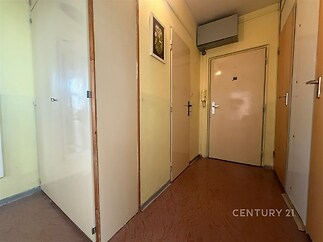 Úzká chodba s linoleem, bílé dveře a starší omítka, obytné prostory čekající na rekonstrukci, jasné stěny dodávají světlost prostoru.