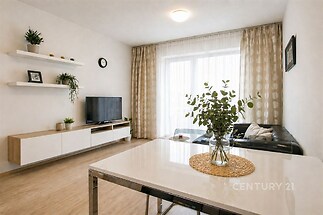 Světlý obývací pokoj s parketovou podlahou, velkými okny a moderním nábytkem. Clean lines a minimalistický design vytváří elegantní atmosféru.