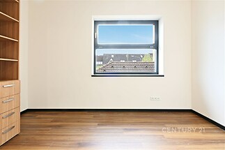 Světlý pokoj s parketovou podlahou, vestavěnými skříněmi a velkým oknem, moderní design v neutrálních tónech, vhodný pro různé využití.