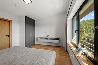 Světlá ložnice s parketovou podlahou, velkými okny a moderní vestavěnou skříní nabízí krásný výhled na přírodu.