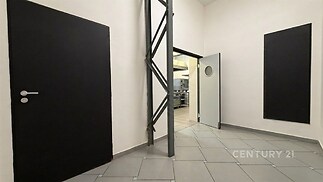 Vstupní chodba s keramickou dlažbou a moderními dveřmi, vedoucí do průmyslové kuchyně, světlé stěny a minimalistický design