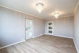 Světlý obývací pokoj s parketovou podlahou, moderními lustry a bílými dveřmi, ideální pro milovníky minimalistického stylu