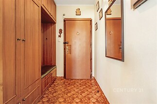 Vstupní hala s dřevěnými vestavěnými skříněmi, dlažbou a velkým zrcadlem na zdi poskytuje praktické úložné možnosti a útulný styl.