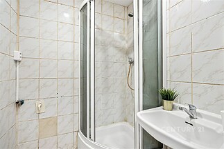 Koupelna s bílými kachličkami, sprchovým koutem a umyvadlem. Kompaktní prostor s moderním vybavením, ideální pro menší byt.