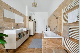 Prostorná koupelna s moderní dlažbou, dvěma umyvadly a velkým zrcadlem, světlé obklady a topný žebřík dotvářejí elegantní styl.