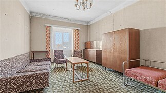 Obývací pokoj s retro nábytkem, kobercem a velkými okny, potřebuje rekonstrukci, nabízí potenciál pro světlý a moderní interiér.