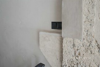 Útulný detail stěny s betonovou omítkou a kamenným obkladem, zvýrazňující moderní průmyslový styl interiéru.