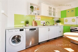 Prostorná kuchyň s bílými skříňkami, zelenými obklady a dlažbou. Obsahuje myčku, pračku a vestavěné police. Světlé a moderní zařízení.