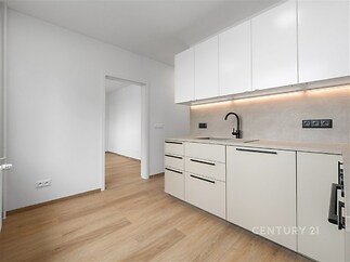 Moderní kuchyň s parketovou podlahou, světlými vestavěnými skříněmi a elegantními spotřebiči, nabízí otevřený prostor a kvalitní provedení.