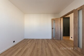 Prázdný pokoj s dřevěnou podlahou, moderními dveřmi a bílými stěnami, ideální pro zařízení podle vlastního vkusu.