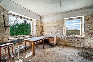 Světlá místnost s kamennými stěnami, dřevěnými okny a betonovou podlahou, ideální pro rekonstrukci a vytvoření stylového obytného prostoru.
