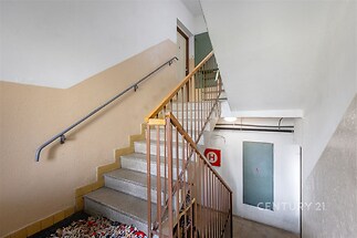 Opravené schodiště v bytovém domě s kovovým zábradlím, texturovanou omítkou a dlažbou na schodech, zabezpečený vstup do patro.