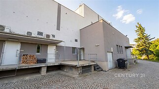 Světlý dvůr s moderní fasádou, dlážděným povrchem a kovovými zábradlími, nabízí prostor pro parkování a usnadňuje přístup k budově.