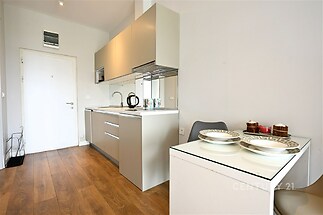 Moderní kuchyň s parketovou podlahou a světlým nábytkem, vedle kompaktní jídelní kout, nabízí moderní design a efektivní využití prostoru.