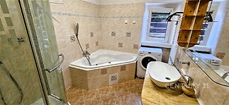 Koupelna s rohovou vanou, proskleným sprchovým koutem a dlažbou v hnědém odstínu, doplněná moderním umyvadlem na dřevěné desce