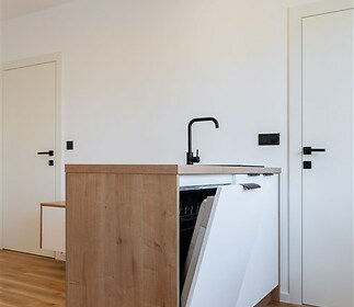 Moderní kuchyň s parketovou podlahou a světlým dřevem, vybavená vestavěnou myčkou a minimalistickým designem.