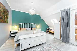 Světlá ložnice s moderním stylem, dřevěnou podlahou a velkými okny, poskytuje útulný prostor pro relaxaci.