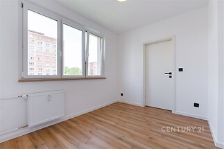 Světlý pokoj s parketovou podlahou a velkými okny, moderní styl, bílá stěna a dveře, ideální pro vytvoření osobního prostoru