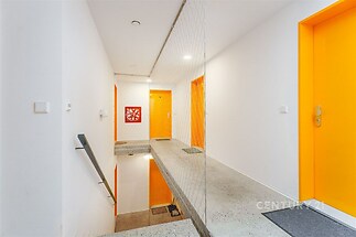 Průchod s moderní betonovou podlahou, světlými stěnami a výraznými oranžovými dveřmi, vytváří svěží a atraktivní vstupní prostor.