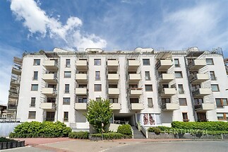 Přední pohled na moderní renovovaný bytový dům s balkony a světlou fasádou, doplněný zelení a upravenou předzahrádkou.