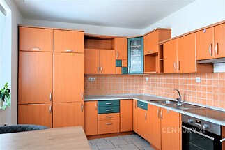 Moderní kuchyň s dřevěnými skříňkami, dlažbou a vestavěnými spotřebiči, ideální pro světlé prostory.