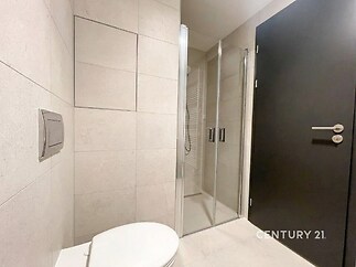Moderní koupelna s dlažbou, proskleným sprchovým koutem a vestavěným WC, čistý a elegantní design, světlé materiály zvýrazňují prostor.