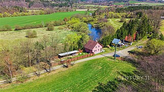 Červený rodinný dům na venkově, obklopený zelení a rybníkem, v klidné a malebné lokalitě.