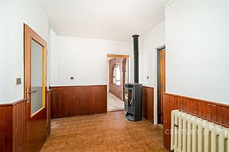 Vstupní hala s keramickou dlažbou, dřevěným obložením stěn a krbovými kamny, vedoucí do cihlové chodby.