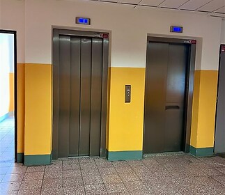 Společné prostory s dlažbou a dvěma výtahy, moderní stav, žluté zdi.