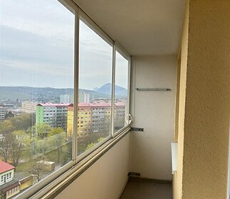 Uzavřený balkon s dlažbou, velkými okny a výhledem na městskou krajinu, ideální pro relaxaci a odpočinek, v dobrém stavu.