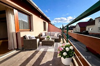 Prostorný balkon s dlažbou, moderní venkovní nábytek a výhled do klidné ulice. Velká okna zajišťují dostatek světla do interiéru.