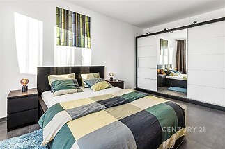 Světlá ložnice s moderní dlažbou, vestavěnou skříní a velkým zrcadlem, které opticky zvětšuje prostor a doplňuje elegantní interiér.