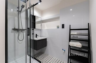 Moderní koupelna s proskleným sprchovým koutem, bílými dlaždicemi a dlažbou s geometrickým vzorem, elegantní černé prvky dodávají styl.