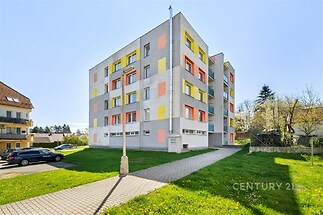 Čtyřpodlažní bytový dům s barevnou fasádou, udržovaným trávníkem a parkovacími místy, v klidném rezidenčním prostředí.
